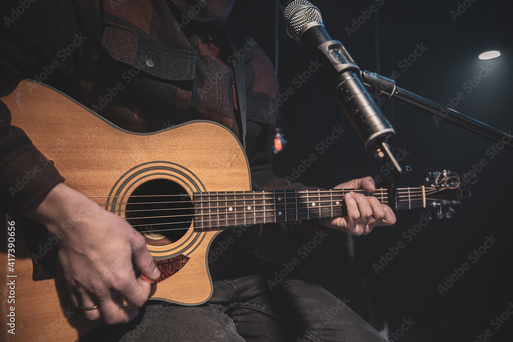 Close up a man plays an acoustic guitar in a dark room.