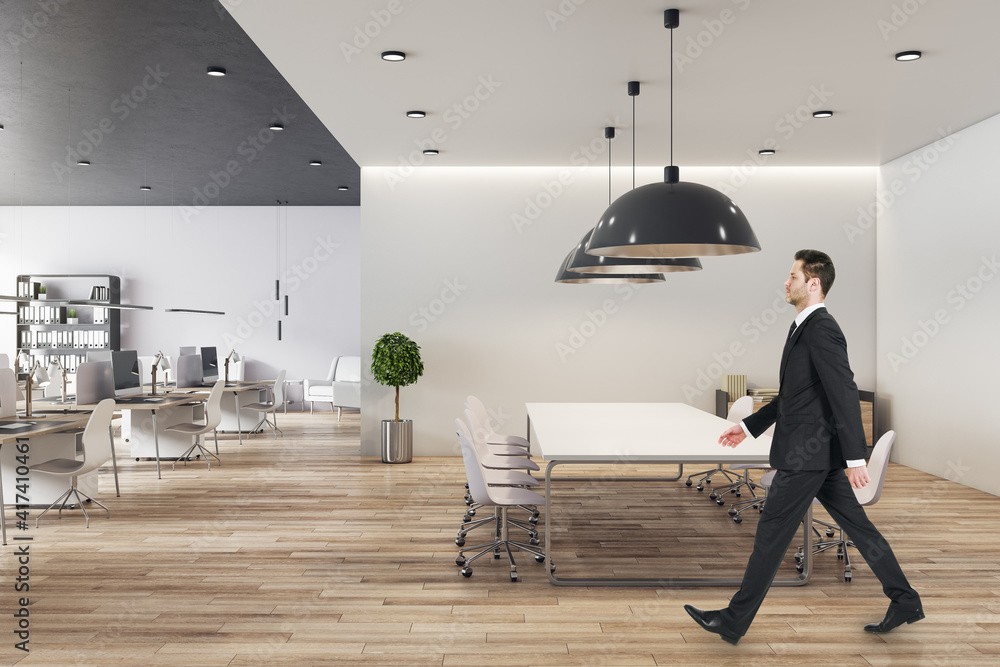 Businessman in black suit goes by big conference table in modern open space office with wooden floor