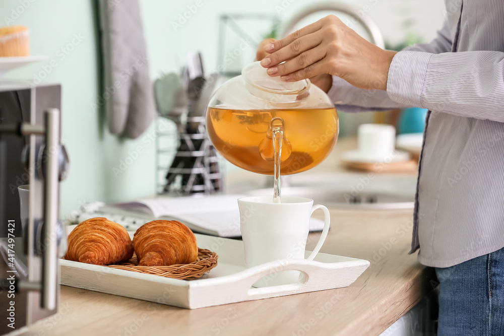Woman pouring tea from teapot into cup in kitchen