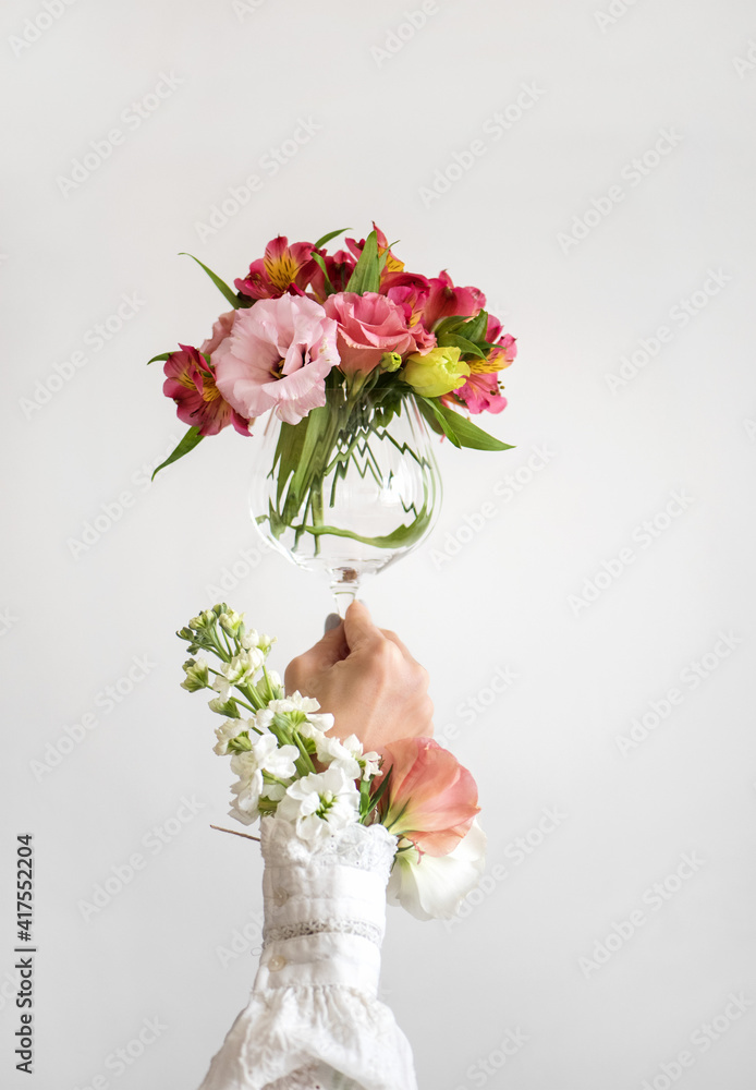 酒杯里装满了新鲜的粉红色、红色和白色的春花，手里拿着一个穿着白色上衣的女人，白色