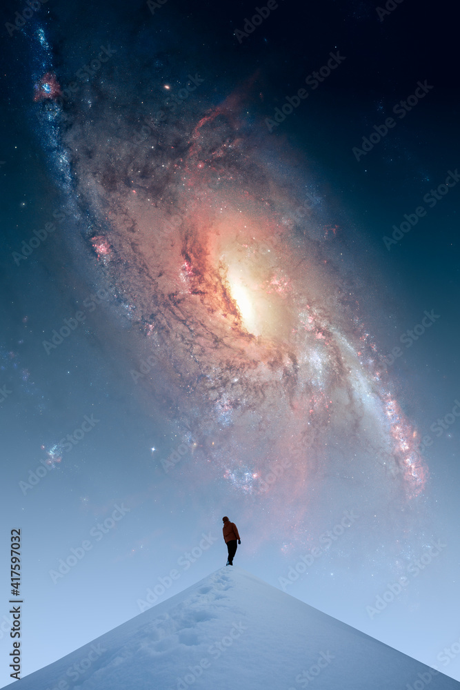 一个人站在雪山上，看着夜空中一个巨大的螺旋星系