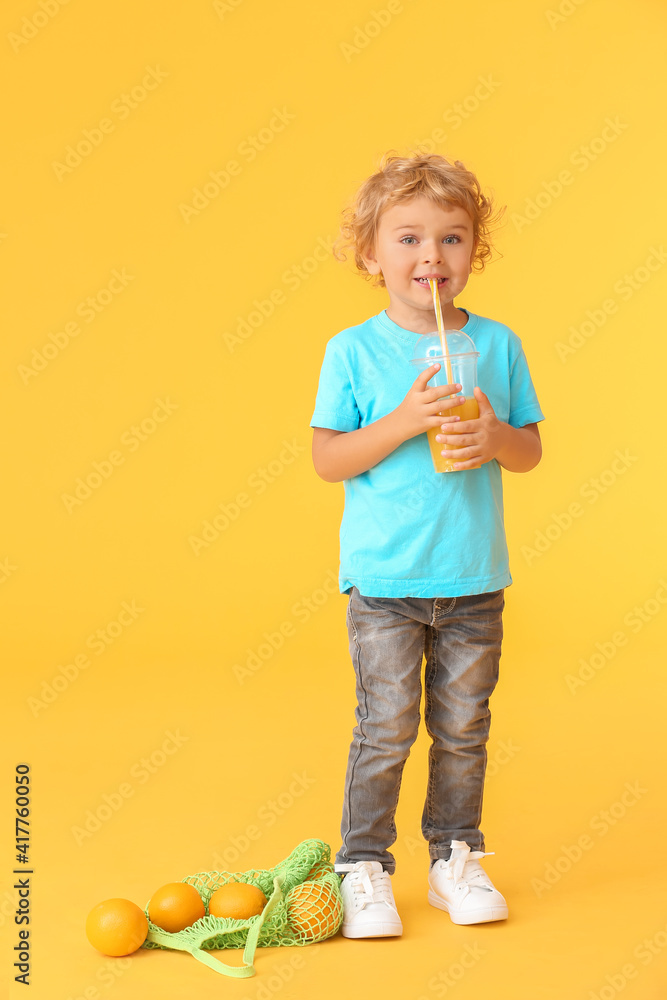 可爱的小男孩在彩色背景下喝橙汁
