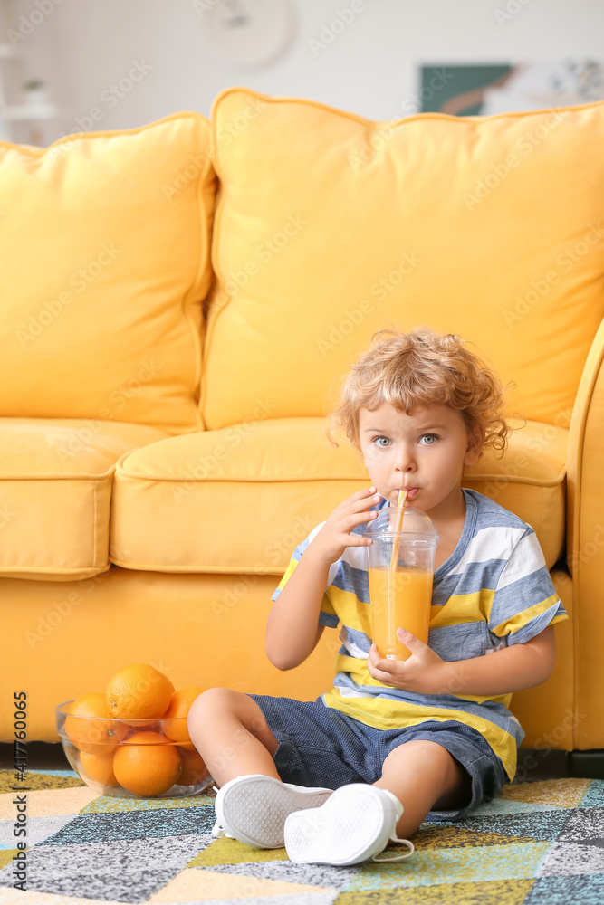 可爱的小男孩在房间沙发附近喝橙汁