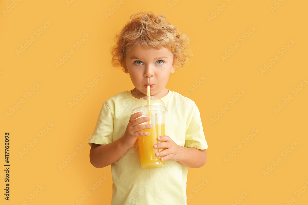 可爱的小男孩在彩色背景下喝橙汁