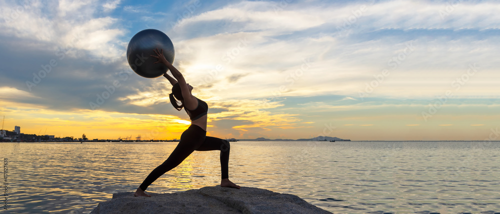 剪影健康女性瑜伽球平衡身体锻炼重要冥想和在岩石上练习