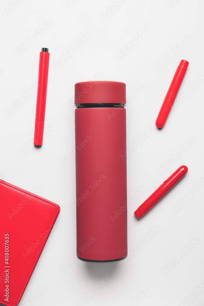 Modern thermos with notebook and pens on light background