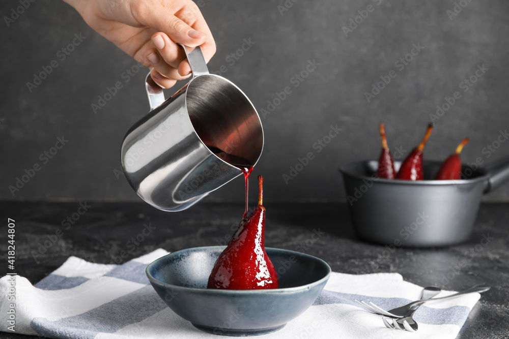 Woman pouring wine sauce onto sweet poached pear on dark background