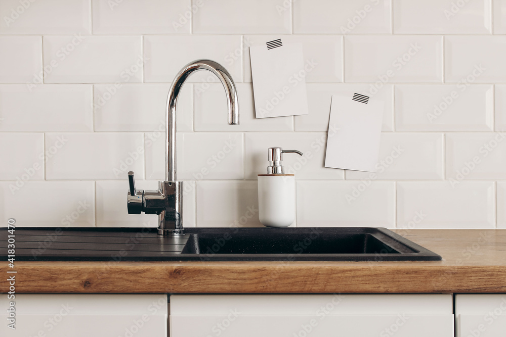 现代厨房静物。白色瓷砖墙上贴着空白纸卡模型。带水龙头的空白水槽