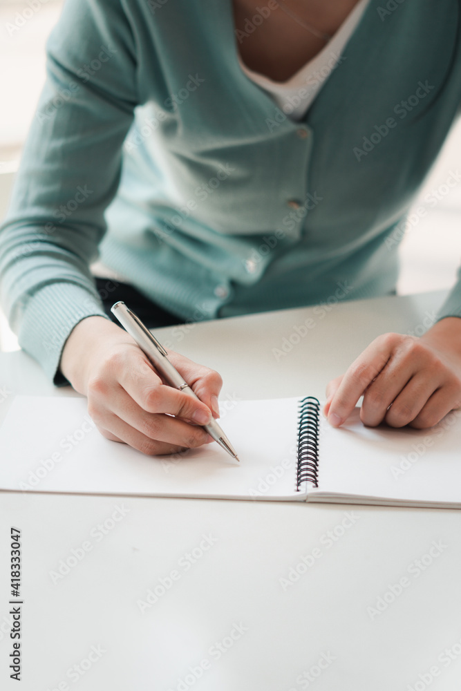 商界女性在电脑上工作，用笔在记事本上写字，用智慧计算财务报表