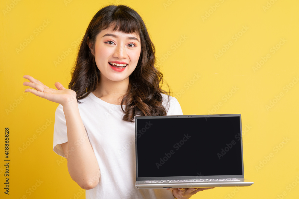 年轻的亚洲女人拿着黄色背景的笔记本电脑