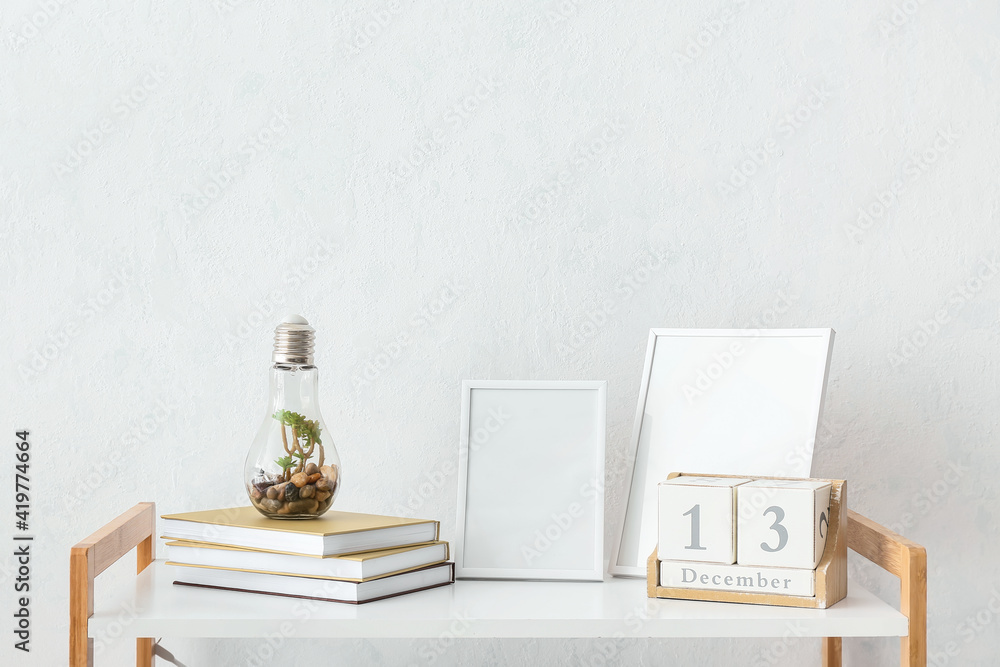 桌子上靠着浅色墙壁摆放着一摞书、日历和空白相框