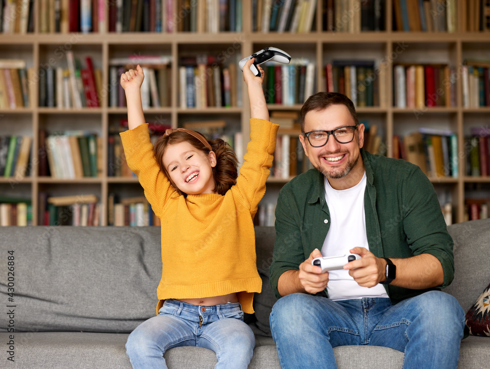 欣喜若狂的家庭父女在家和爸爸玩电子游戏庆祝成功