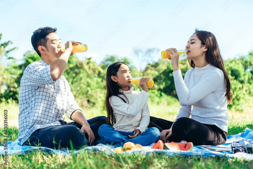 快乐的亚洲家庭正在花园里野餐，和女儿一起喝瓶装橙汁
