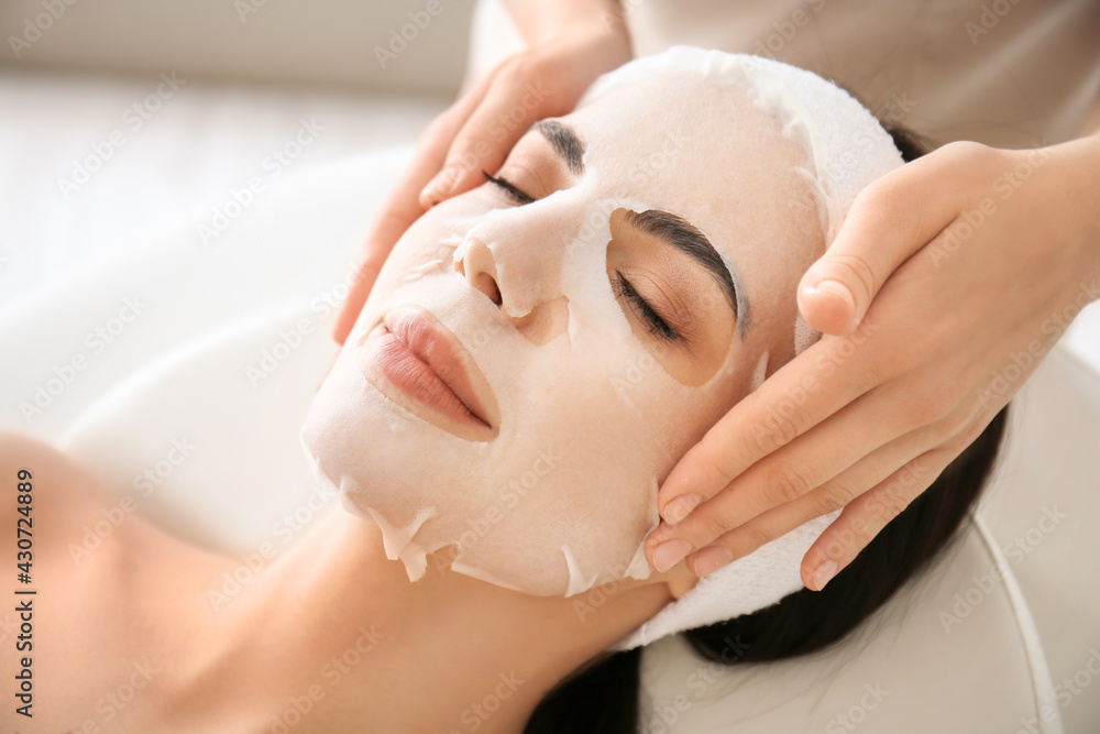 Cosmetologist applying sheet mask on womans face in beauty salon