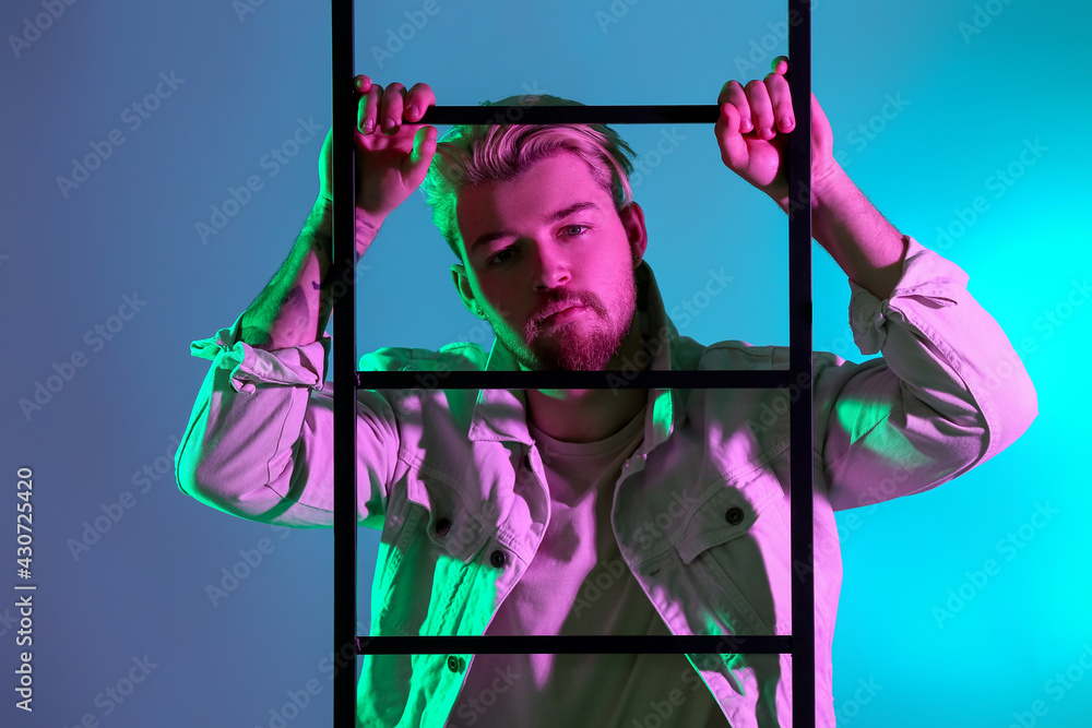 Toned portrait of handsome young man with ladder on color background