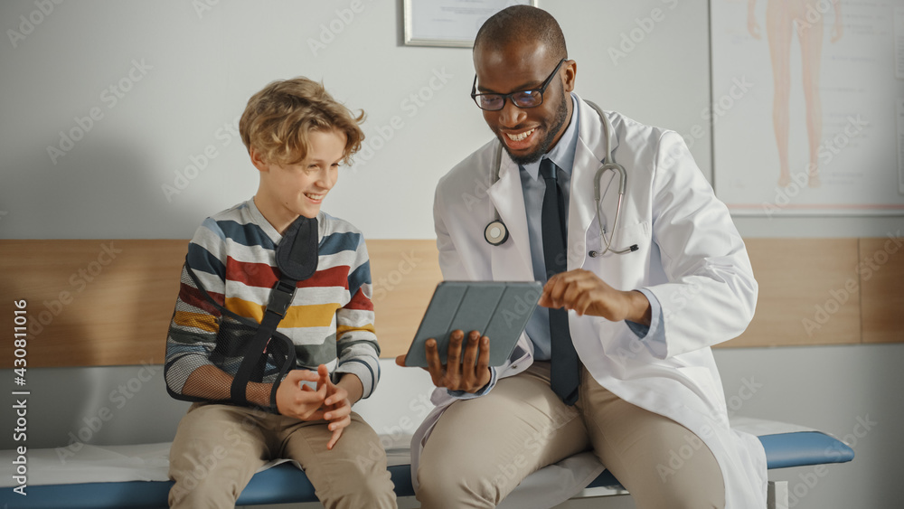 Friendly African American Family Doctor Talking with a Young Boy with Arm Brace and Showing Test Res