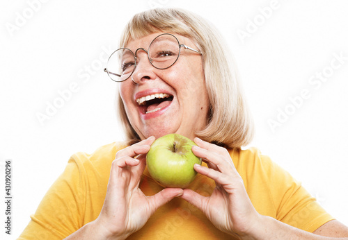 Food, health and old people concept: Portrait of senior woman wearing yellow shirt and glasses holdi