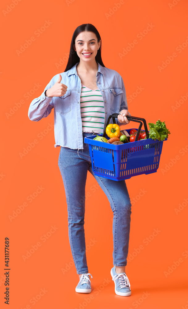 年轻女子拿着购物篮，在彩色背景上竖起大拇指