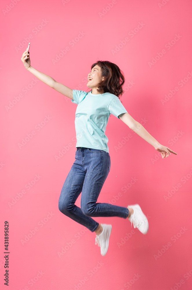 年轻的亚洲女孩拿着手机跳了起来，背景上表情欢快
