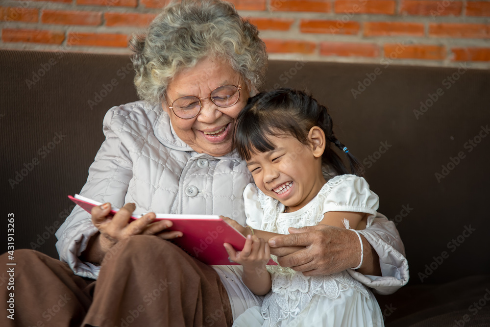 快乐亚洲祖母在家给孙女读童书，祖母教她读boo