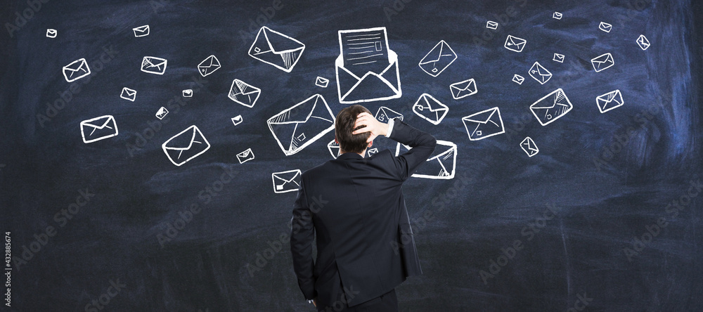 沉思的商人看着写有信件和信封的黑板的电子邮件营销概念