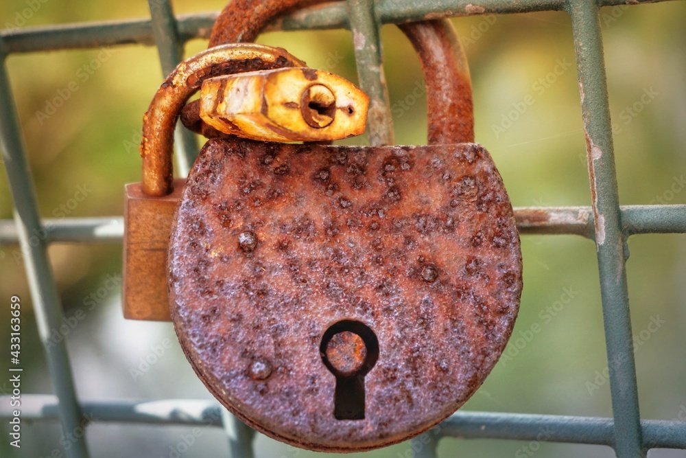 old rusted love lock with two other locks hanging on fence