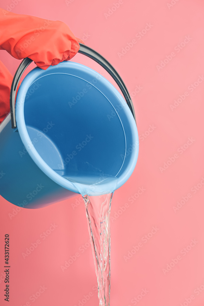 Woman pouring water from bucket on color background