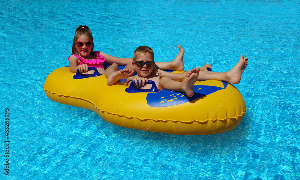 男孩和女孩在室外游泳池的充气浮子上。