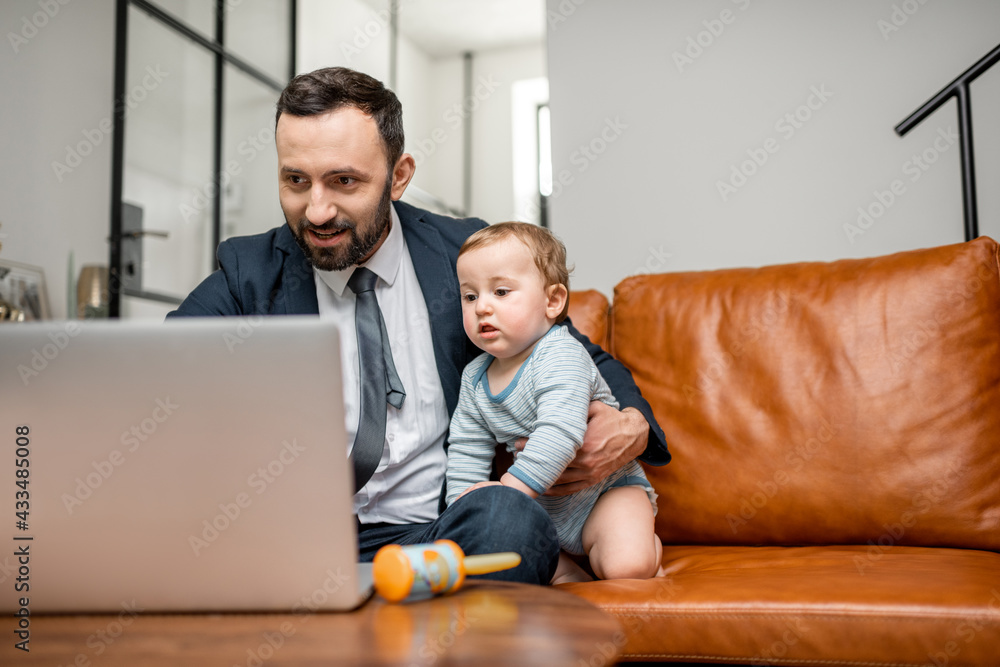 年轻的商人父亲在家里用笔记本电脑工作，同时照顾刚出生的儿子。多任务处理