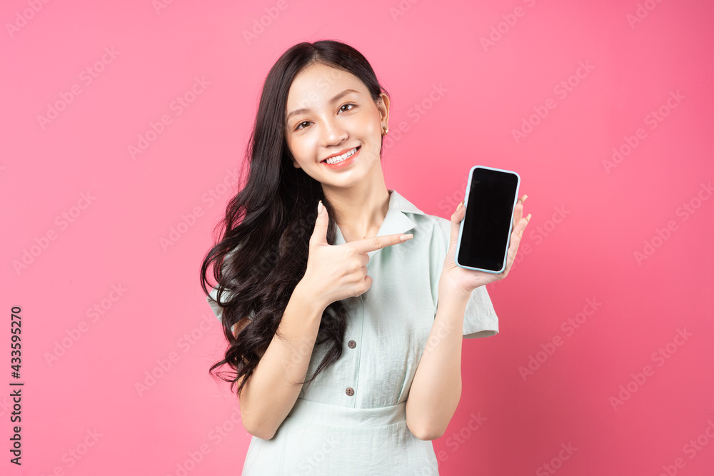 年轻的亚洲女人手里拿着手机，用顽皮的表情指着手机