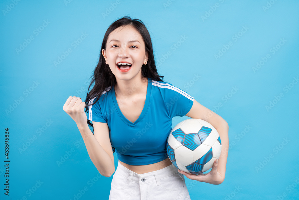 漂亮的亚洲女人拿着蓝色背景的足球摆姿势