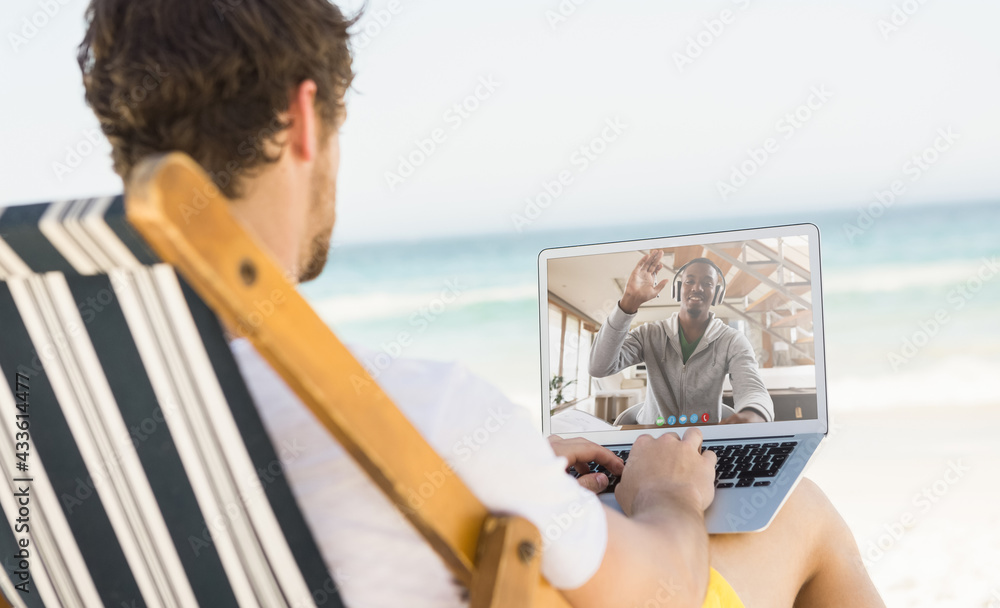 Caucasian man relaxing on beach having video call using laptop