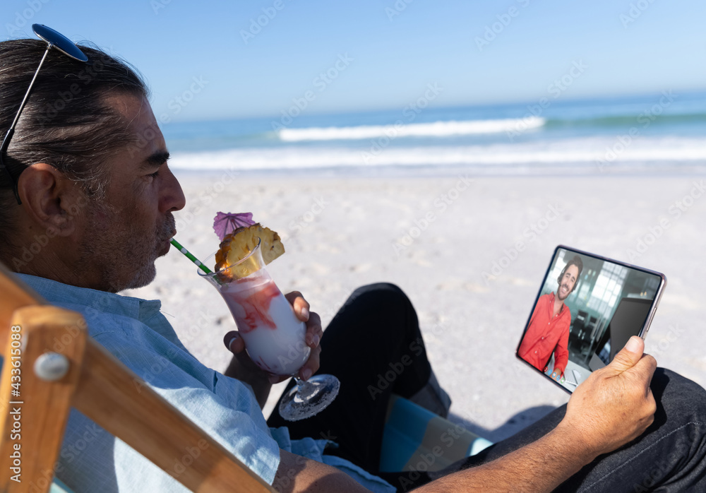 高加索男子在海滩上喝酒放松，用平板电脑进行视频通话