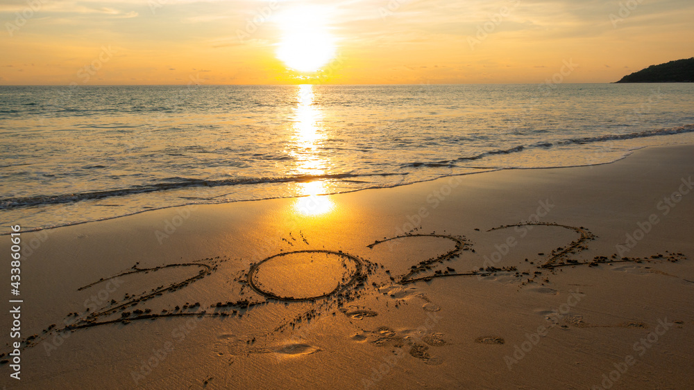 2022年新年快乐，在海滩上用波浪和日落的天空书写2022年的数字