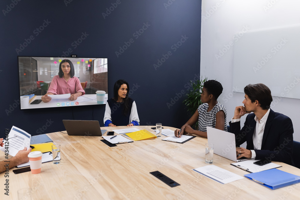 一群不同的商业同事在会议室的屏幕上与女商人进行视频通话