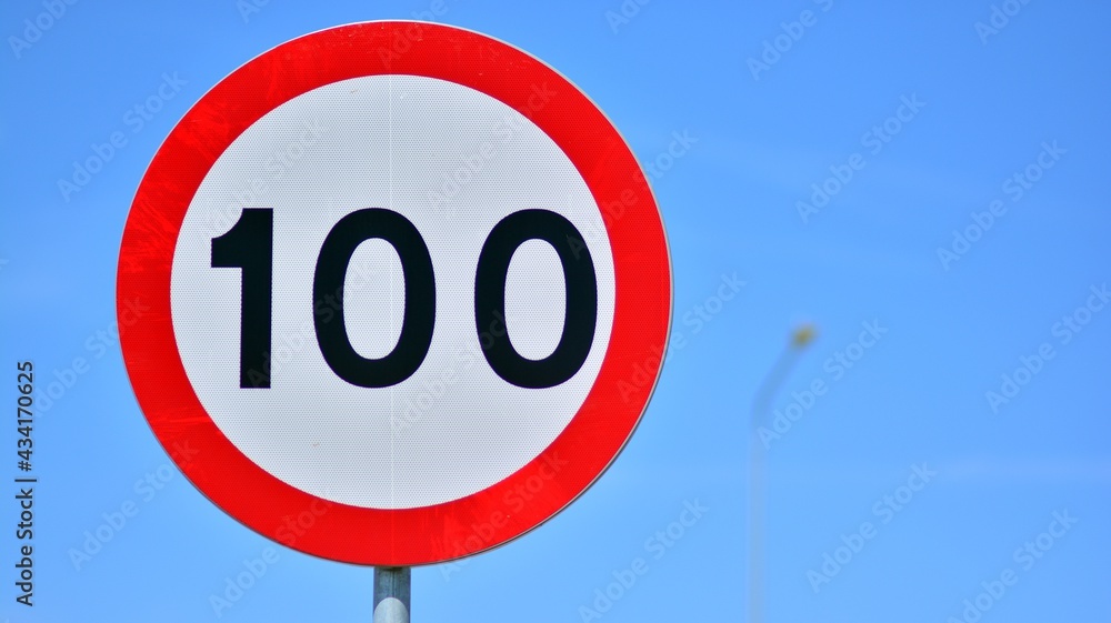 Road sign on a highway  indicates a speed limit of 100 km per hour. Red circle with white center.