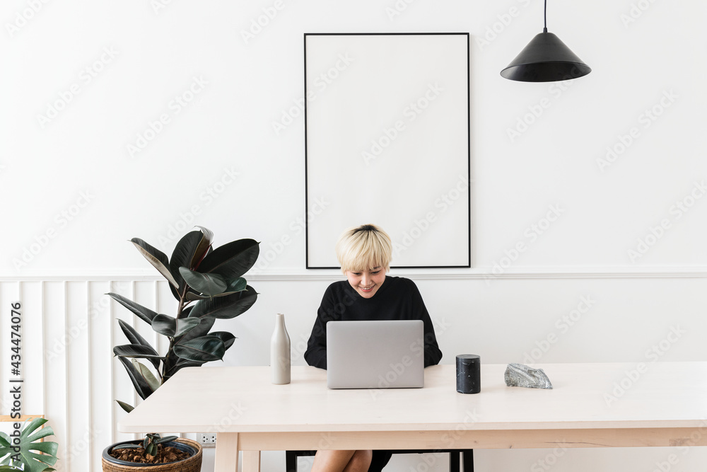 Woman working on her laptop with a blank frame hanging on a wall