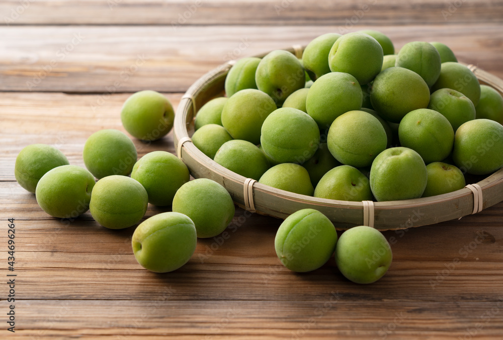 Plum fruit in a bamboo colander placed in the wooden background.