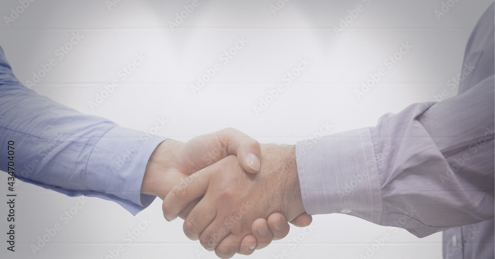 Mid section of two businessmen shaking hands against spot of light against grey background