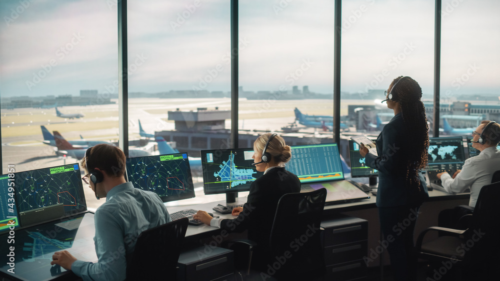 多样化的空中交通管制团队在现代机场塔台工作。办公室里摆满了桌面C