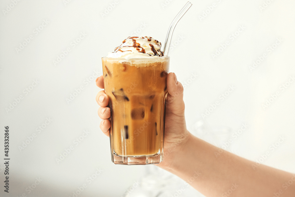 女性手拿一杯美味的冰咖啡，背景为浅色，特写