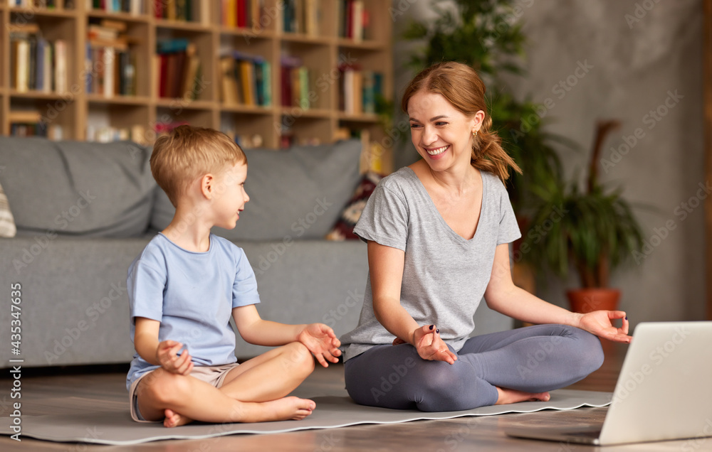 健康的家庭母子在家里一起冥想，同时在笔记本电脑上上在线瑜伽课