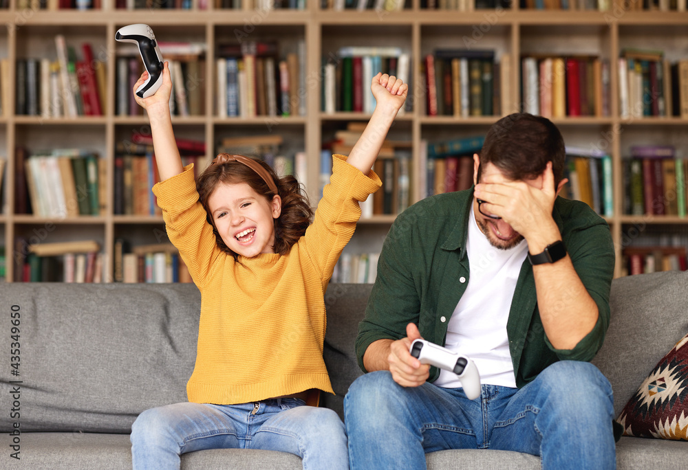 Happy girl celebrating victory while playing video games with dad at home