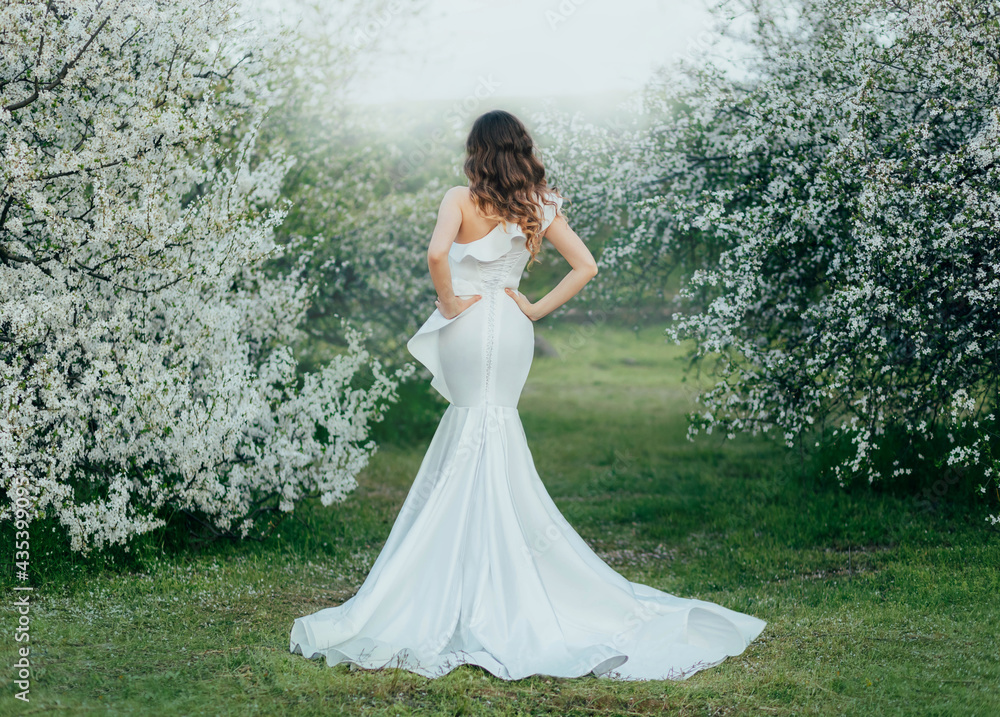 Silhouette of mysterious fantasy woman in long white elegant dress walks in green spring cherry gard