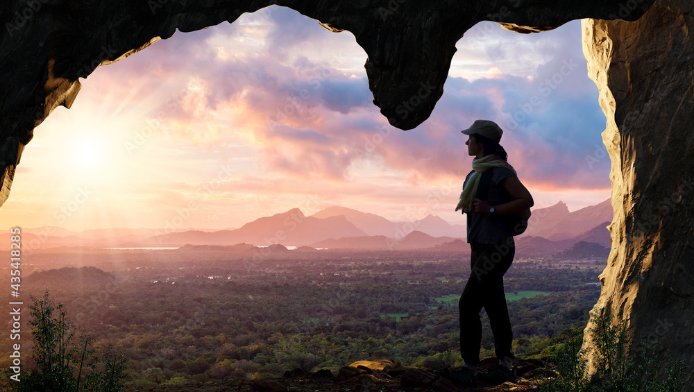 Silhouette of female hiker looking at sunset landscape  from cave.