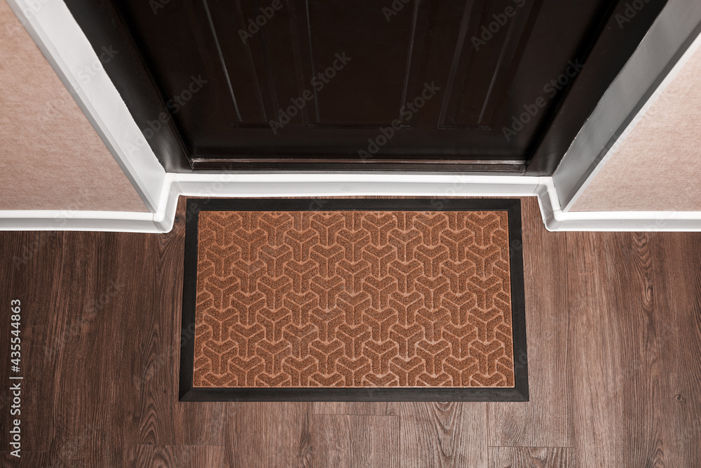 Blank doormat before the dark door in the hall. Top view of mat on wooden floor. Mockup for your des