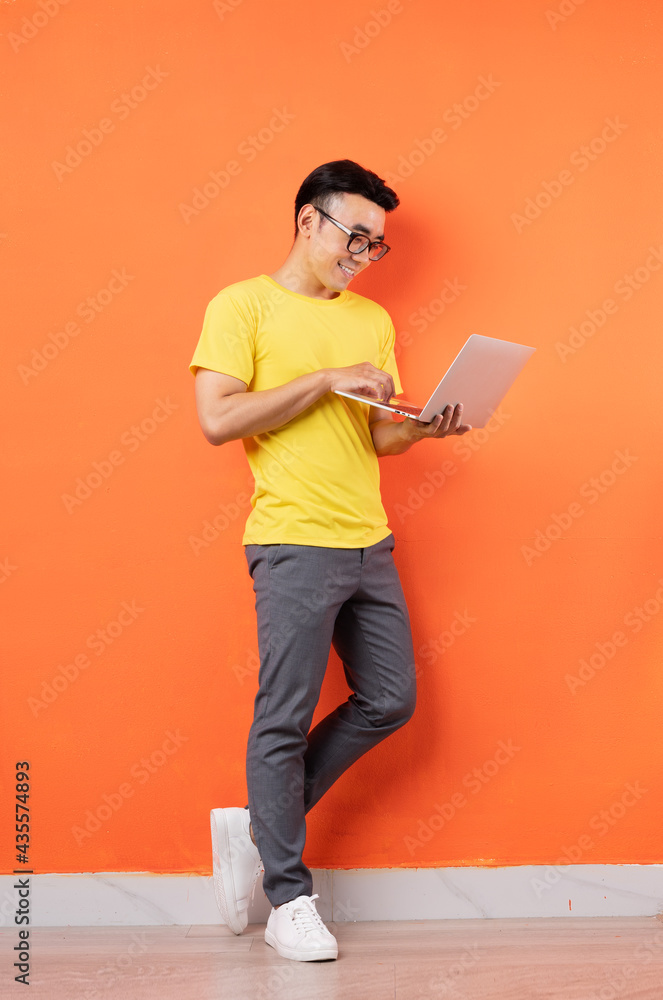 Full body photo of Asian man in yellow shirt on orange background