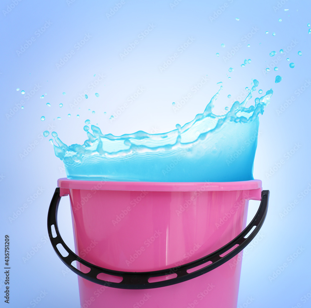 Plastic bucket with water splashes on color background