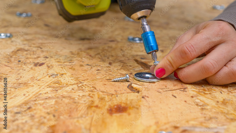 特写：一名妇女用电钻将一个金属垫圈固定在胶合板上。