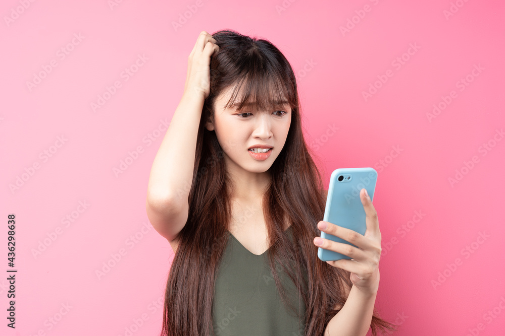 漂亮的年轻亚洲女孩在粉色背景下使用手机